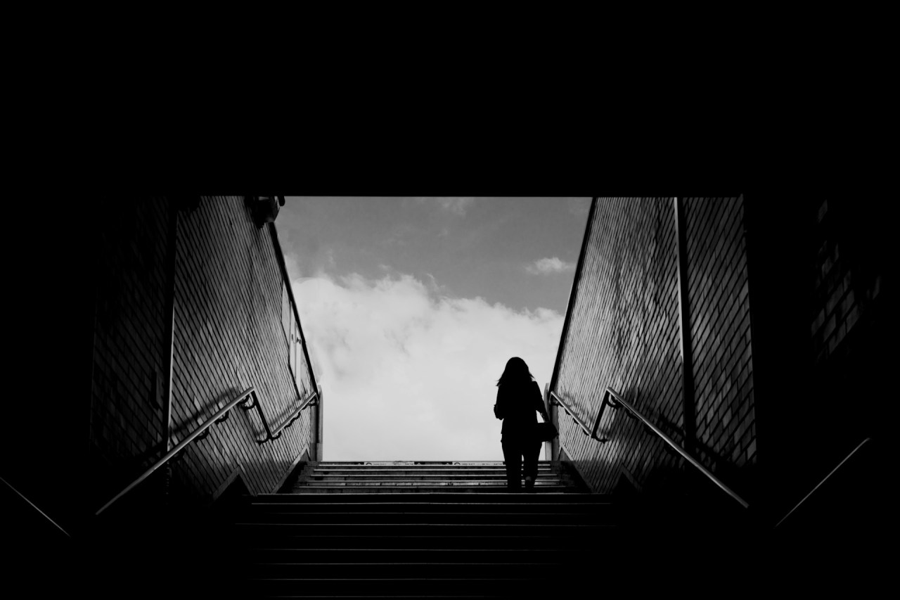 Black and white image of a person standing in a dark tunnel, representing perseverance, failure, and continuing forward after setbacks.