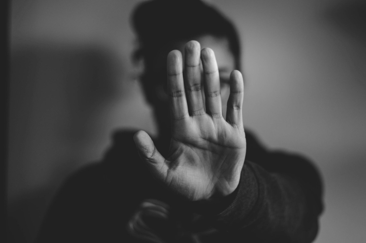 Black and white photo of a person holding up their hand, representing boundaries, disengagement, and protecting your energy.