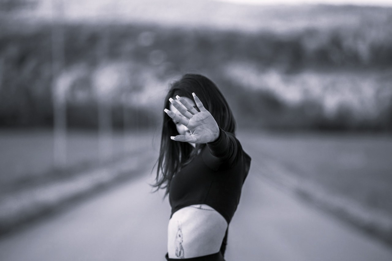 Woman standing alone on a road with her hands covering her face, representing how fixed ideas about ourselves can limit who we become.