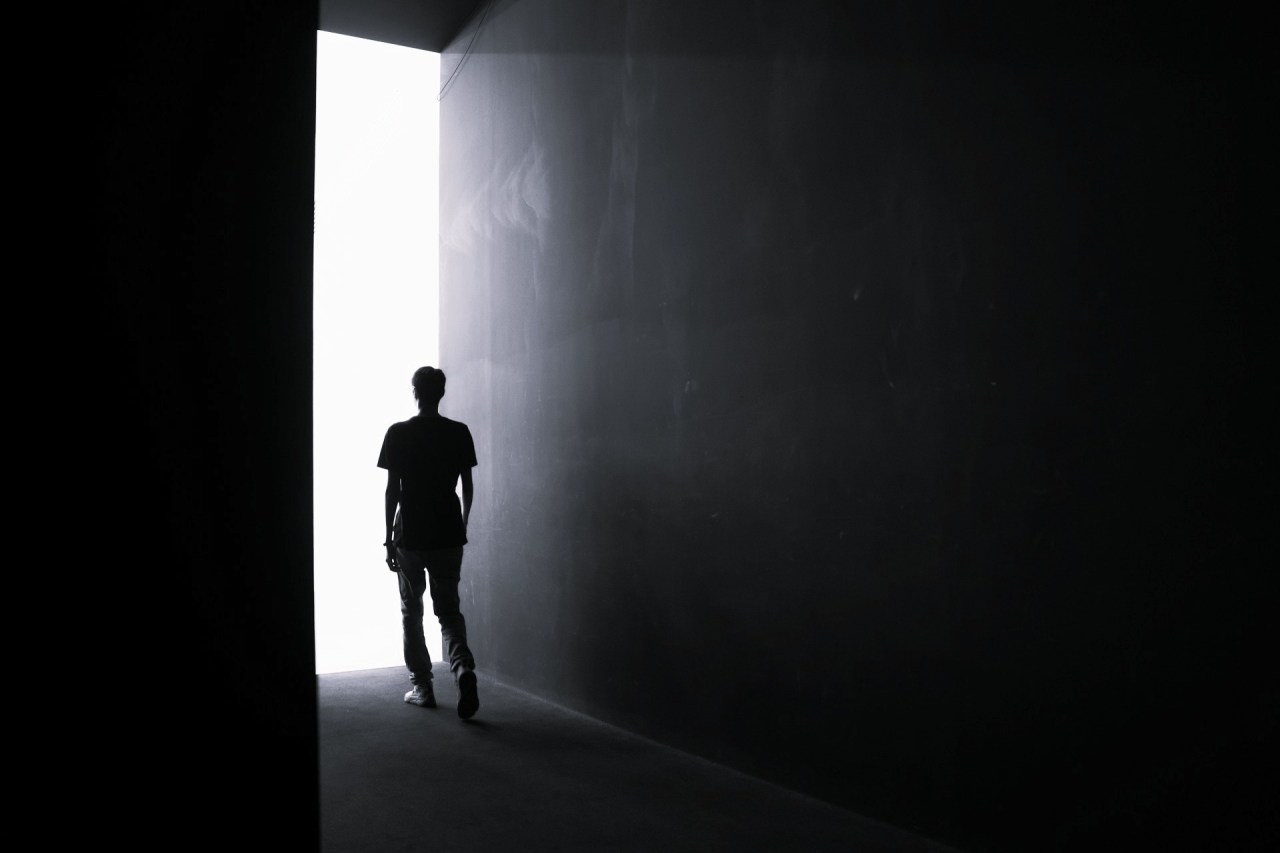 Black and white image of a person standing in an open doorway surrounded by darkness, representing choice, possibility, and discernment.