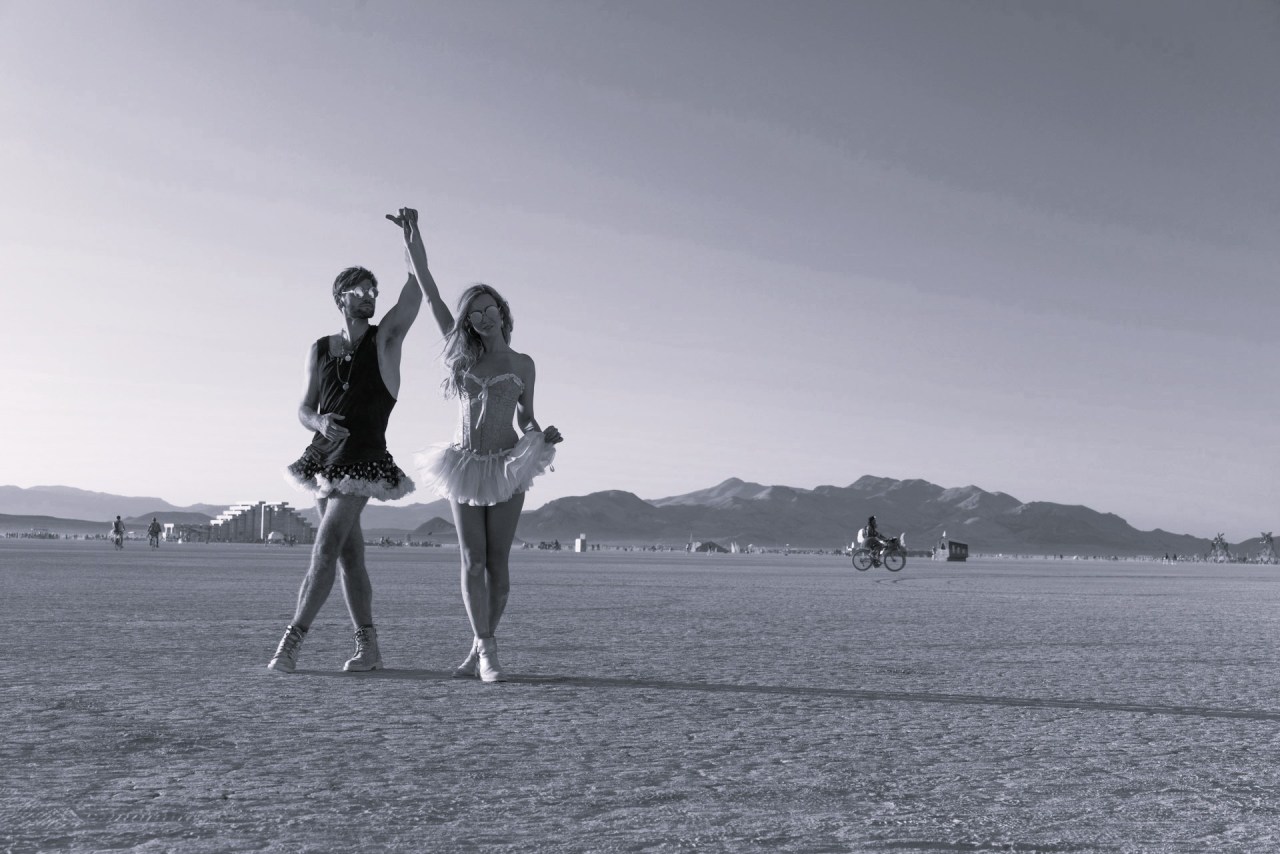 Black and white image of two friends running together on a beach, representing friendship, joy, celebration, and sharing life’s happy moments.
