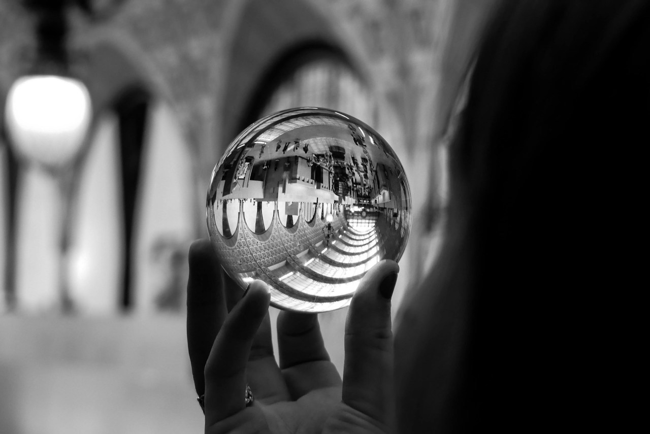 Black and white image of a person looking through a magnifying glass, representing perspective, dreams, progress, and recognizing how far you’ve come.