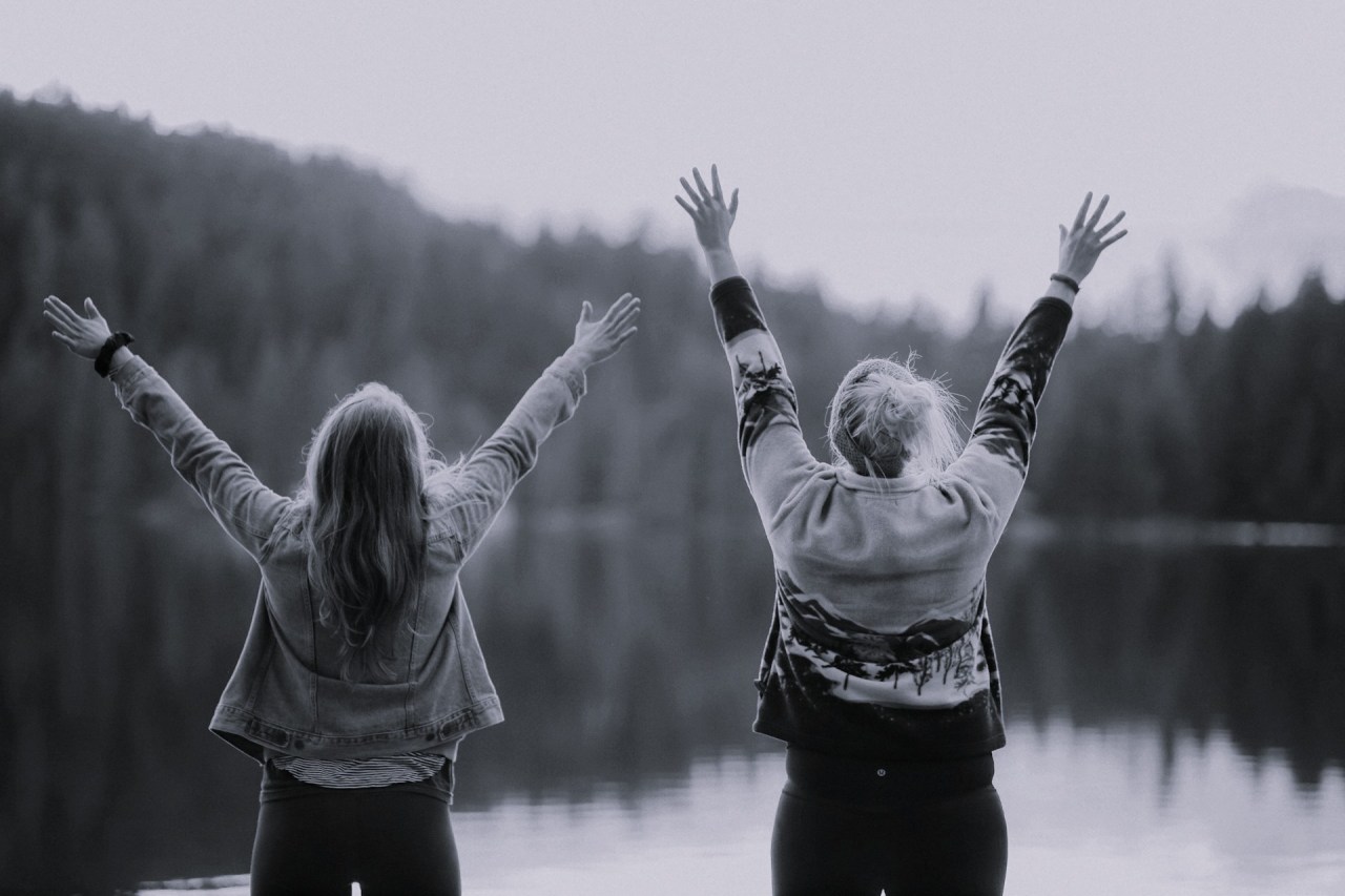 Two women standing by a lake with their arms raised together in celebration.