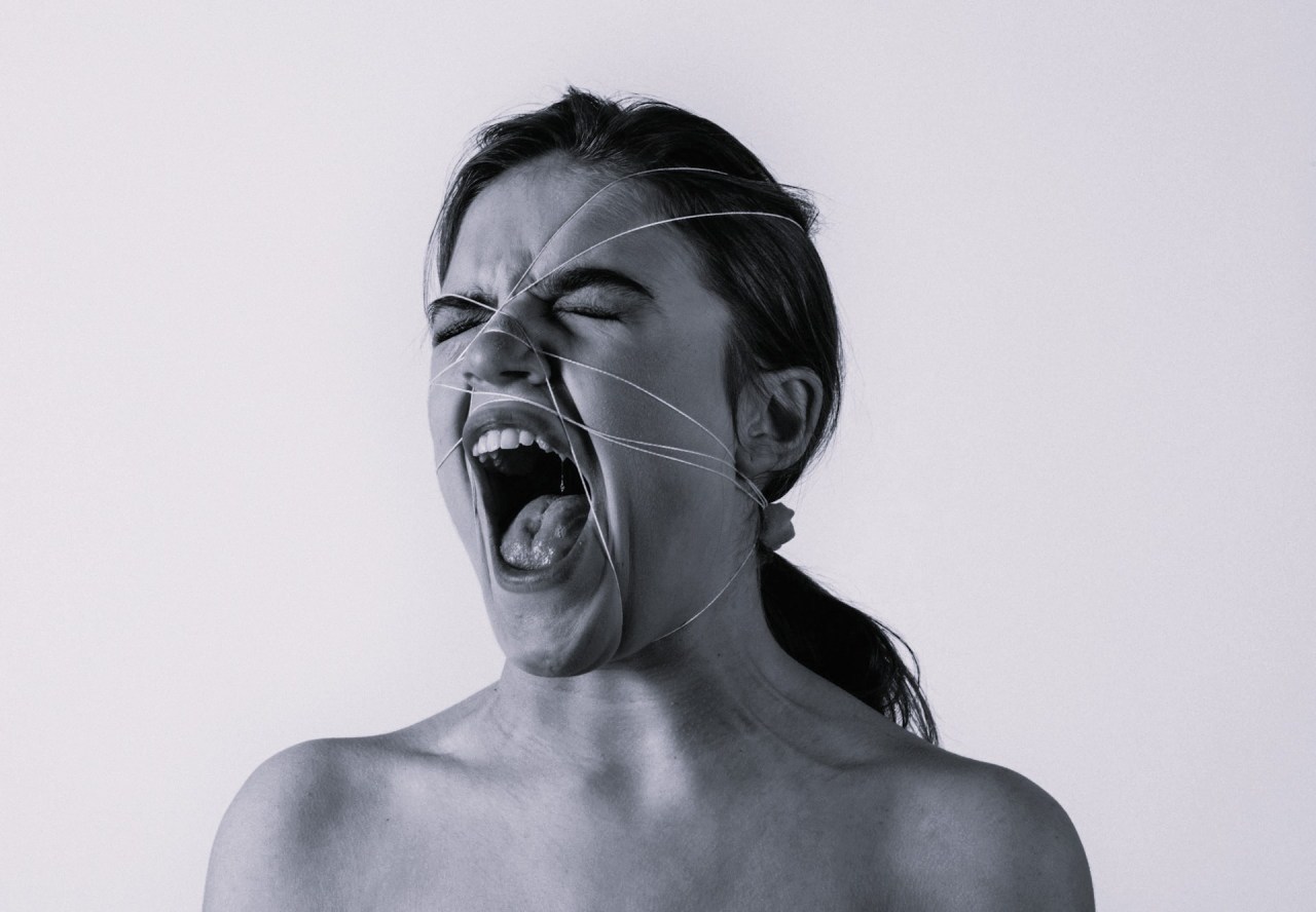 Black-and-white photograph of a woman with her eyes closed and mouth wide open, expressing an intense emotional reaction.