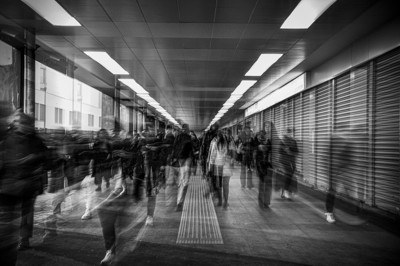 Black-and-white long-exposure photograph of a crowd moving through a busy underground pedestrian corridor.