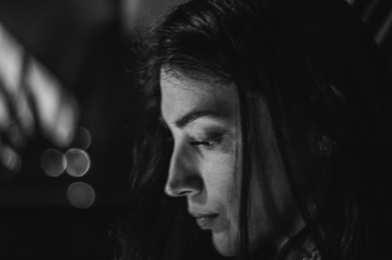 Black-and-white photograph of a woman looking downward with a thoughtful, somber expression.