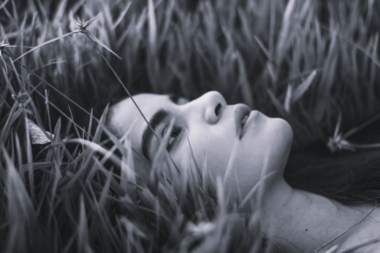 Black and white image of a woman lying in the grass with her eyes closed, reflecting on memory, loss, and letting go of something that once mattered.