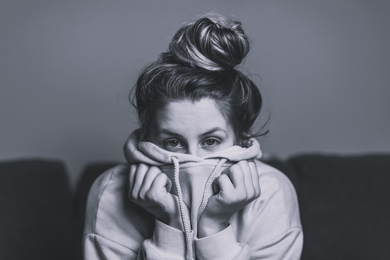 Black and white image of a woman partially covering her face with her sweater, representing fear, uncertainty, and the vulnerability of stepping into something you want.